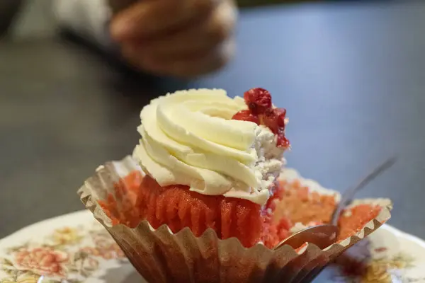 Beyaz kâğıt üzerinde kırmızı bisküvi ve beyaz kremalı bir pasta var. Birisi küçük bir ısırık almış..