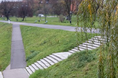 Şehrin içinden akan nehrin manzarası. Nehrin kıyısında binalar ve ağaçlar görülebilir. Arka planda ormanla kaplı bir dağ var..