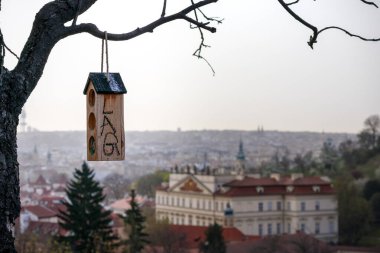 a birdcage hanging from a tree and a large building with a red roof and a white tower can be seen in the distance. clipart