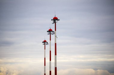 Üç uzun, kırmızı-beyaz anten, gri, bulutlu gökyüzüne doğru yükseliyor..