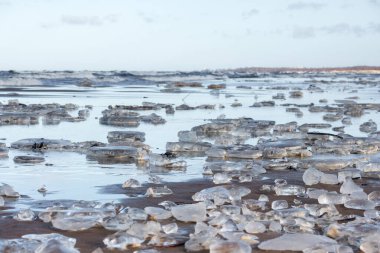 a wide landscape with lots of ice floes lying on water and sandy land, with the sky in the background. clipart