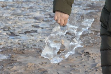  İnsan eli, buz ve kum blokları ile delikleri ve arka plan manzaralı saydam buz bloğunu tutuyor..