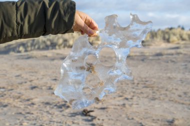  İnsan eli, buz ve kum blokları ile delikleri ve arka plan manzaralı saydam buz bloğunu tutuyor..