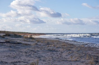 Arkasında deniz olan kumlu bir sahil ve bulutlu bir gökyüzü..