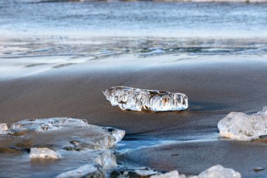 Arkasında su olan kumlu bir sahilde buz parçaları..