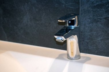 Krom musluk beyaz lavaboda, koyu bir arka planda..