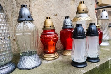 Altın süsleme ve çiçek süslemeleri gibi dekoratif unsurlara sahip büyük, beyaz bir vazo ya da kap, arka planda yeşillik görülebilen bir kaideye yerleştirilir..