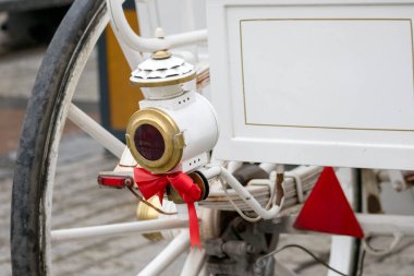 Atın ön bacağı ve kahverengi-beyaz paltosunun bir kısmı görülebilir, kırmızı püsküllü siyah kayış süslemesinin yanında ve arka planda güvercinler görülebilir..