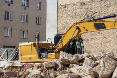 Büyük, sarı bir kazıcı moloz ve binaların arasında bir inşaat sahasında bulunuyor..