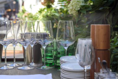 Arka planda yeşillik ve çiçeklerle birlikte açık hava etkinliği için hazırlanmış bardaklar, tabaklar ve diğer yemeklerle dolu bir masa..