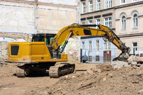 Büyük, sarı bir kazıcı, arka planda eski binalar ve kum ve moloz yığınları bulunan bir inşaat sahasında bulunuyor..