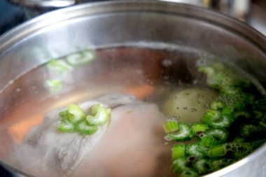 Büyük metal bir tencerede kaynayan havuç ve kereviz gibi domuz inciği ve sebzeler..