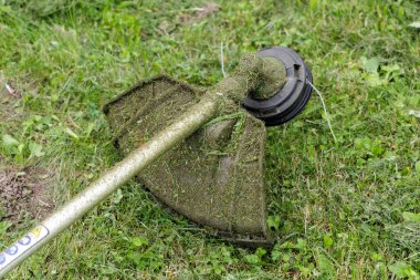 Çim biçme makinası, çim biçme makinesiyle kaplı, kullanımdan sonra çimlerin üzerinde duruyor, bahçe bakımını ve açık hava işini sembolize ediyor.