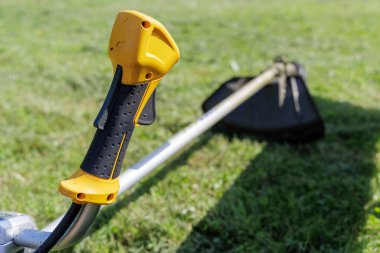 Bir tel budayıcının sarı ve siyah sapı parlak yeşil bir çimenlik üzerinde dinlenen araç ile belirgin bir özelliktir, kullanıma hazır veya sonra.