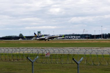  Riga Uluslararası Havalimanı 'ndan kalkan bir hava baltık uçağı, arka planda, Baltık havacılığının büyümesini sembolize eden hangarlar bulunduruyor..