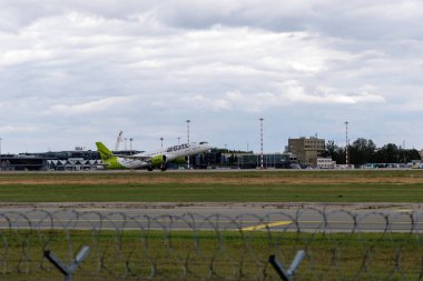  Riga Uluslararası Havalimanı 'ndan kalkan bir hava baltık uçağı, arka planda, Baltık havacılığının büyümesini sembolize eden hangarlar bulunduruyor..