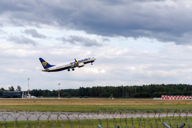  Riga Uluslararası Havalimanı 'ndan kalkan bir hava baltık uçağı, arka planda, Baltık havacılığının büyümesini sembolize eden hangarlar bulunduruyor..