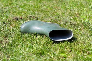 Tek bir yeşil lastik yağmur botu parlak güneş ışığı altında canlı yeşil bir çimenlikte yatay olarak yatar..