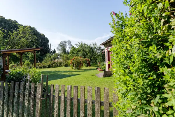 Büyüleyici bir kır bahçesi, yemyeşil çimenleri, kırmızı güller, ve küçük kırmızı bir bina, kırsal ahşap bir çitin üzerinde görülmüş..