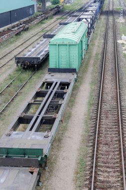 Birçok yük vagonunun yakın çekim görüntüsü, aralarında belirgin yeşil ve düz vagonların da bulunduğu, bir demiryolu alanındaki birden fazla demiryolu hattında..