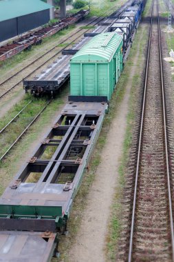 Birçok yük vagonunun yakın çekim görüntüsü, aralarında belirgin yeşil ve düz vagonların da bulunduğu, bir demiryolu alanındaki birden fazla demiryolu hattında..