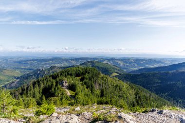 Yoğun yeşil ormanları ve güneşli bir günde açık mavi gökyüzü olan uçsuz bucaksız bir dağ manzarası..