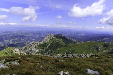 Yuvarlak bir patikası olan kayalık bir dağ sırtının dramatik yüksek açılı görüntüsü, aşağısında bir kasaba bulunan geniş, ormanlık bir vadiye bakıyor..