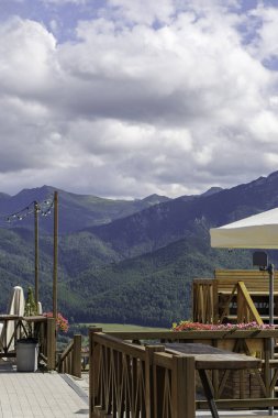 Ahşap mobilyalar ve büyük bir şemsiyeyle muhteşem panoramik bir dağ manzarası olan ferah bir teras..