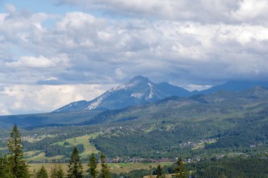 Bir vadideki küçük bir köyün geniş bir görüntüsü, uzakta belirgin bir Tatra zirvesi ve yukarıda güzel bulutlu bir gökyüzü..