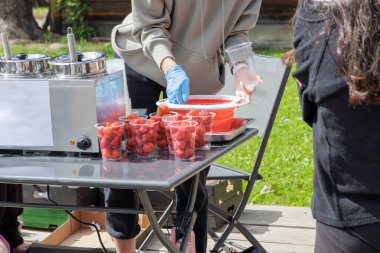 Küçük yuvarlak çörekleri plastik bardaklara servis eden mavi bir eldiven giyen bir insan..