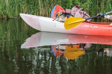 Kürek ve seyahat çantalarıyla bir kanoya yakın çekim, sakin, karanlık bir nehri yansıtıyor, macera için bir hazırlık hissi yakalıyor..
