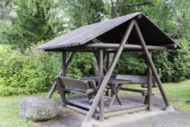  Masası ve bankları olan ahşap bir çardak ağaçlarla ve kırsal bir yolda büyük bir taşla çevrili..