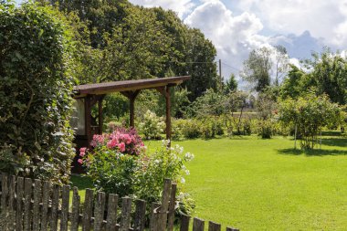 Kırsal ahşap çitleri olan huzurlu bir bahçe manzarası çiçek açan çiçekler ve yeşil çimenli küçük bir çardak..