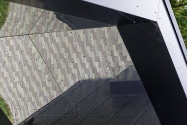 Modern bir binanın ön cephesinin siyah ve aynalı yüzeyinde dokulu gri asfaltın karmaşık, geometrik bir yansıması..