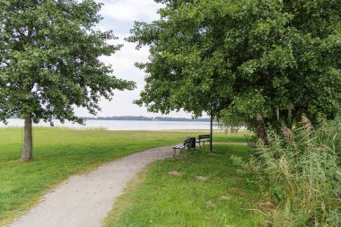 İki park sırasının çakıl yolunun sonunda oturduğu, yoğun yeşil ağaçların çerçevelediği, sakin bir göl manzarası sunduğu resim gibi bir sahne.. 
