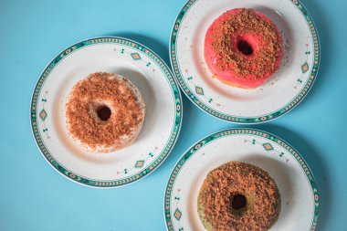 Donuts made by a home industry with the basic ingredients of palm sugar with various kinds of toppings such as chocolate, strawberries, green tea, and sprinkles. photographed flat served on a plate and a turquoise background