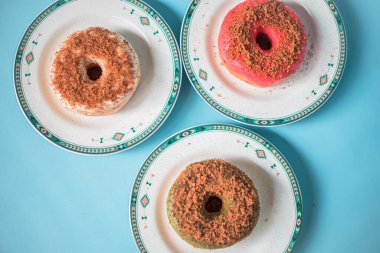 Donuts made by a home industry with the basic ingredients of palm sugar with various kinds of toppings such as chocolate, strawberries, green tea, and sprinkles. photographed flat served on a plate and a turquoise background