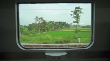 Ride the train sitting by the window looking at the view of the tracks and rice fields outside the window the train is speeding towards its destination