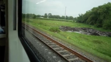 Ride the train sitting by the window looking at the view of the tracks and rice fields outside the window the train is speeding towards its destination