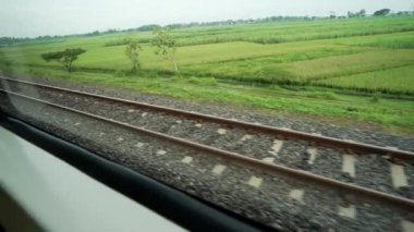 Ride the train sitting by the window looking at the view of the tracks and rice fields outside the window the train is speeding towards its destination