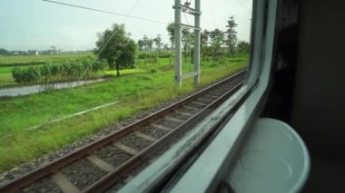 Ride the train sitting by the window looking at the view of the tracks and rice fields outside the window the train is speeding towards its destination