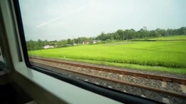 Ride the train sitting by the window looking at the view of the tracks and rice fields outside the window the train is speeding towards its destination