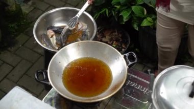 Asian woman's hands are in the process of frying a catfish that has been seasoned and put in a pan of hot oil, frying the catfish to become dry and crunchy in boiling oil