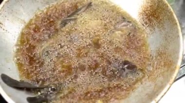 Asian woman's hands are in the process of frying a catfish that has been seasoned and put in a pan of hot oil, frying the catfish to become dry and crunchy in boiling oil