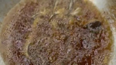 Asian woman's hands are in the process of frying a catfish that has been seasoned and put in a pan of hot oil, frying the catfish to become dry and crunchy in boiling oil