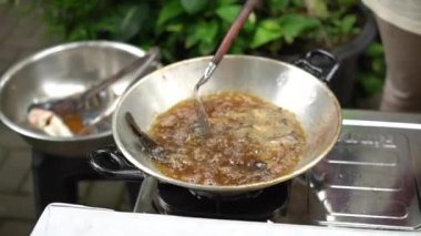 Asian woman's hands are in the process of frying a catfish that has been seasoned and put in a pan of hot oil, frying the catfish to become dry and crunchy in boiling oil
