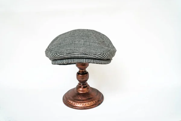 Detail of a scally cap or flat cap, with black and white tweed herringbone pattern mounted on a bronze mannequin head on a white background