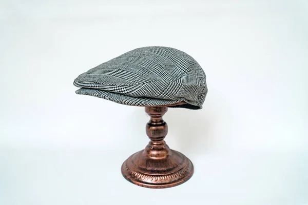 Detail of a scally cap or flat cap, with black and white tweed herringbone pattern mounted on a bronze mannequin head on a white background