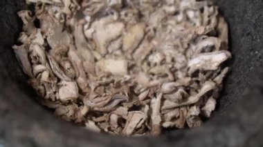 Asyalı kadınların elleri geleneksel bir taş havan topu kullanarak dilimlenmiş baharatları elle toza çeviriyor. Yavaş çekim detayı. El yapımı otlar ve baharatlar.