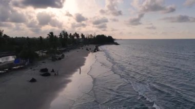 Güneşin kumsaldaki kumları yıkayan deniz dalgalarının üzerinde battığı güzel bir an. Doğu Aceh, Endonezya 'da bozulmamış bir sahilde gün batımının sinematik drone görüntüleri.